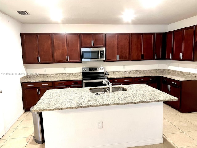 982 SW Alcantarra Blvd, Port St Lucie, FL 34953 - kitchen featuring appliances with stainless steel finishes, dark brown cabinets, light tile patterned flooring, an island with sink, and light stone countertops