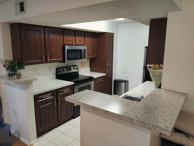 10361 SW 150th Ct Unit 13104, Miami, FL 33196 - kitchen with appliances with stainless steel finishes, a peninsula, light countertops, light tile patterned flooring, and a breakfast bar area