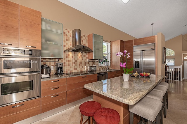 2188 NW 158th Ave, Pembroke Pines, FL 33028 - kitchen featuring appliances with stainless steel finishes, a kitchen bar, vaulted ceiling, wall chimney range hood, and brown cabinets