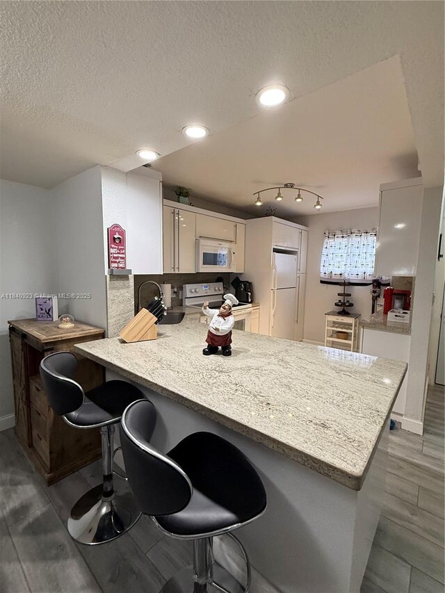 11 Olive Dr Unit E, Hialeah, FL 33010 - kitchen featuring a peninsula, white appliances, white cabinetry, a textured ceiling, and a kitchen breakfast bar