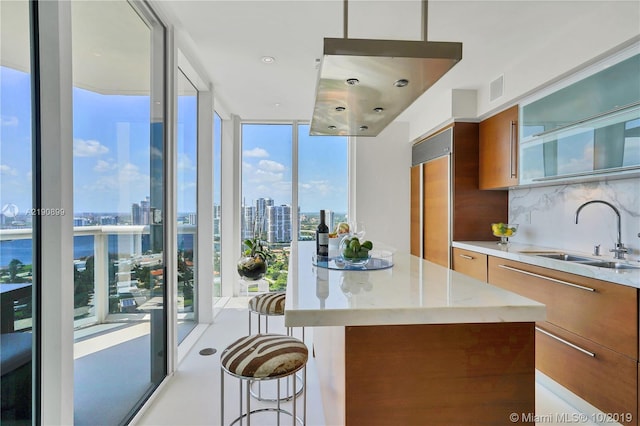 kitchen featuring a kitchen island, a kitchen breakfast bar, sink, decorative backsplash, and a wall of windows