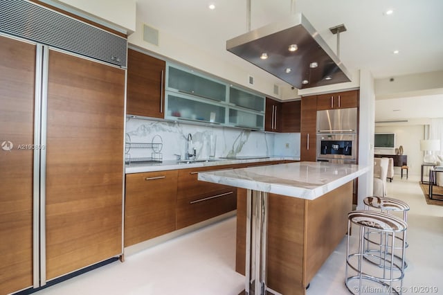 kitchen with backsplash, paneled built in refrigerator, sink, stainless steel fridge, and a spacious island