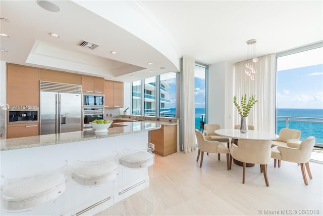 kitchen featuring expansive windows, hanging light fixtures, built in appliances, light stone counters, and a water view