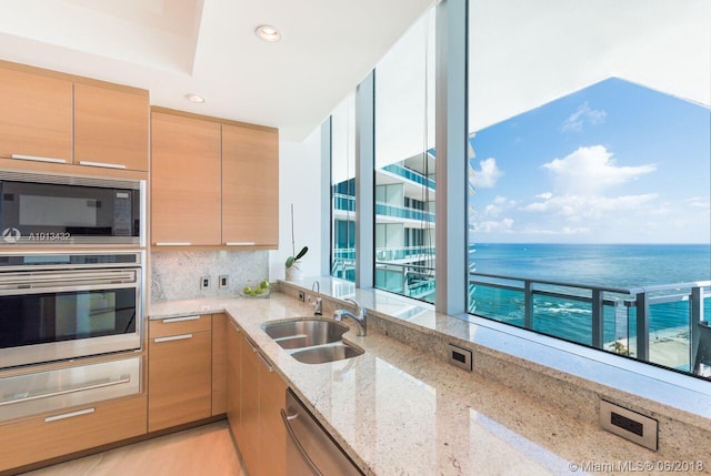 kitchen with sink, light stone counters, a water view, stainless steel appliances, and decorative backsplash