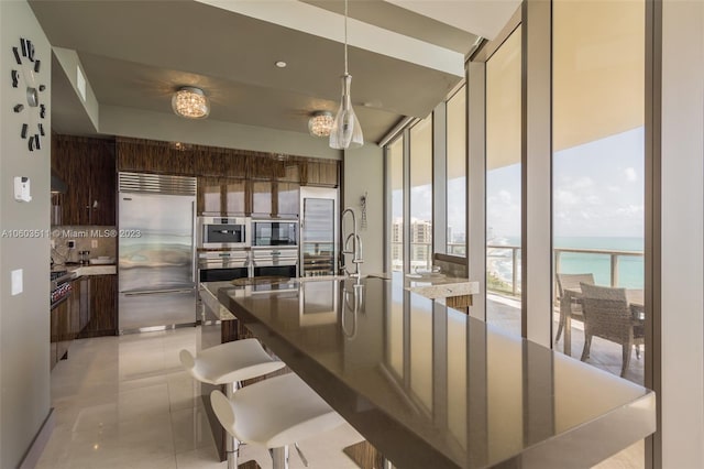 kitchen featuring light tile patterned flooring, built in appliances, a water view, and floor to ceiling windows