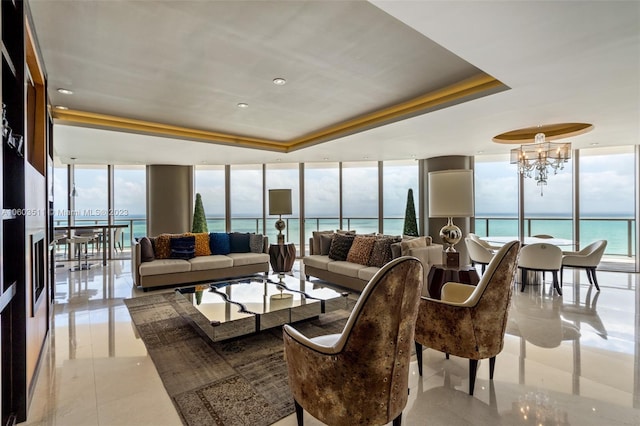 tiled living room with an inviting chandelier, a water view, floor to ceiling windows, and a raised ceiling