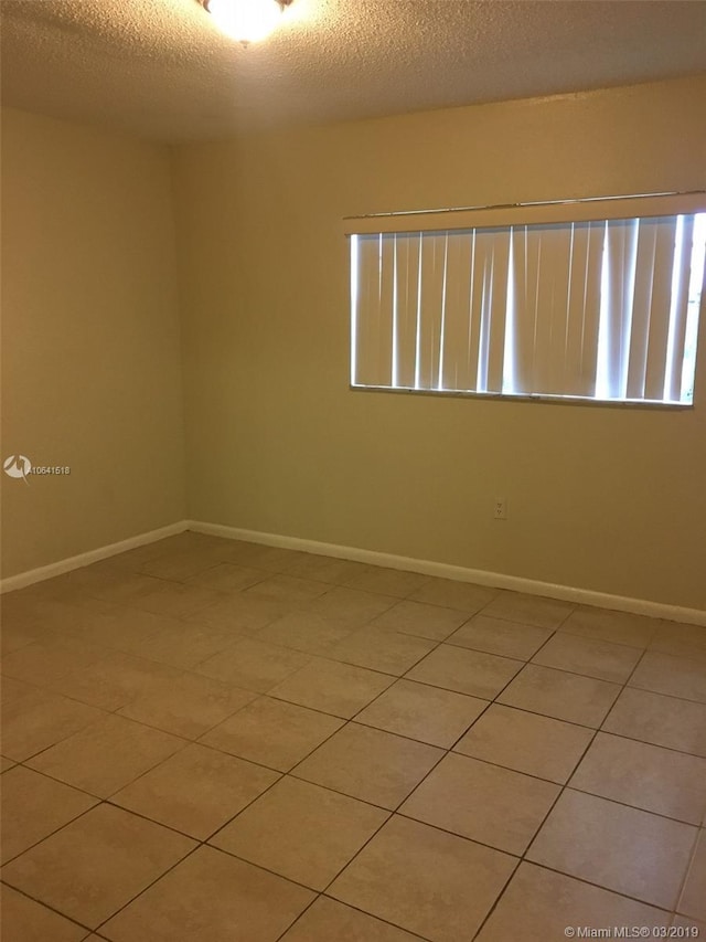 empty room with a textured ceiling and tile patterned flooring