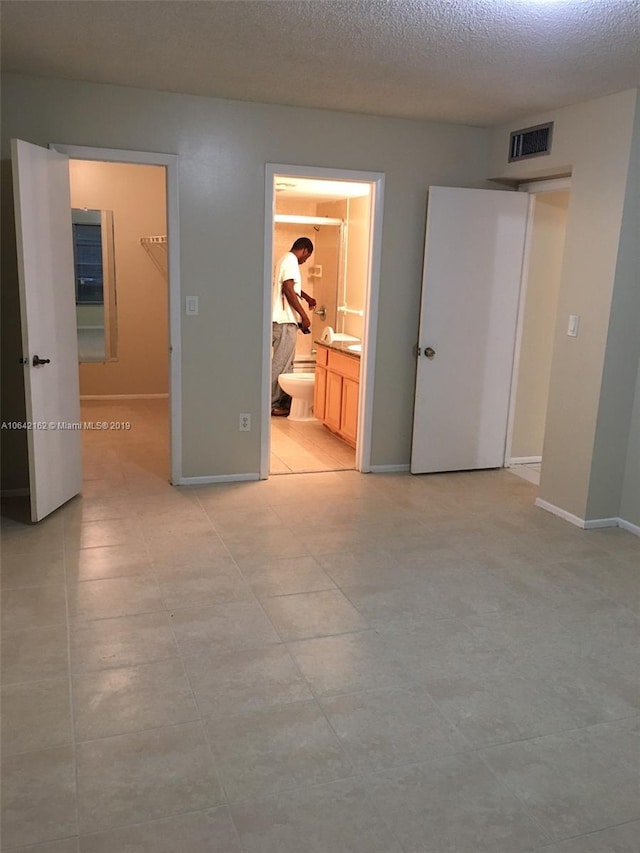 unfurnished bedroom with a closet, light tile flooring, connected bathroom, a textured ceiling, and a spacious closet