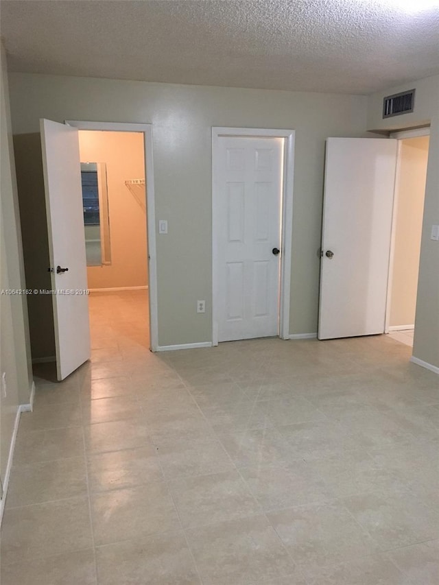 unfurnished bedroom featuring a walk in closet, a textured ceiling, a closet, and light tile floors