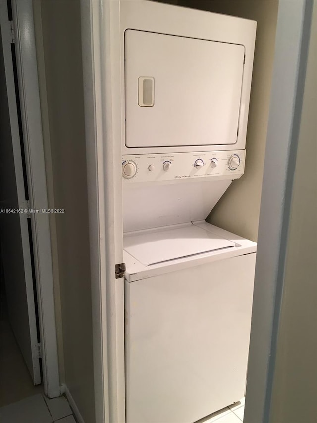 clothes washing area featuring light tile floors and stacked washing maching and dryer