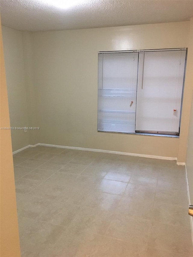 unfurnished room featuring a textured ceiling and light tile flooring