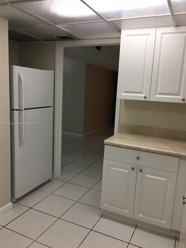 kitchen with a paneled ceiling, white cabinets, white fridge, and light tile floors