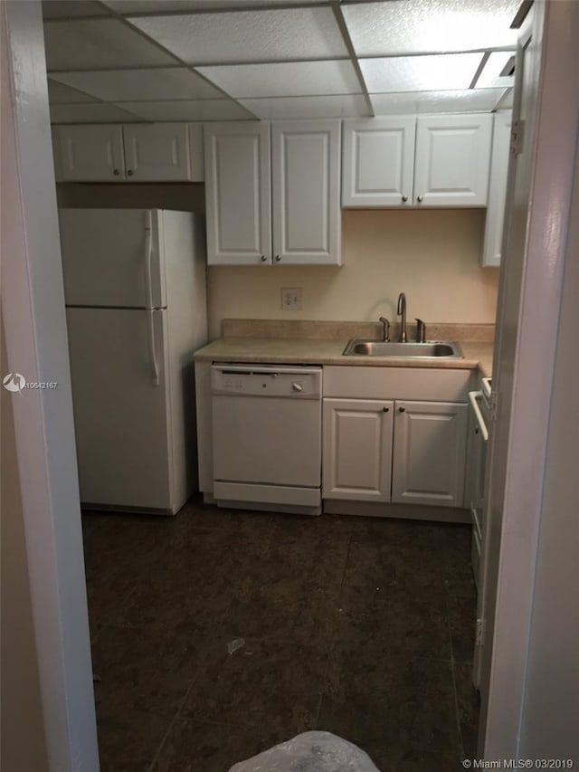 kitchen with a paneled ceiling, white appliances, dark tile flooring, white cabinets, and sink