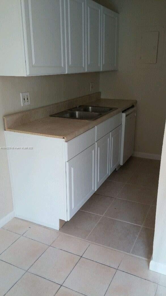 kitchen featuring white cabinetry, sink, white dishwasher, and light tile patterned floors