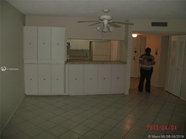 interior space featuring white fridge, ceiling fan, light tile floors, white cabinets, and a textured ceiling