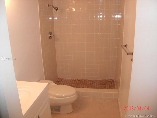 bathroom with toilet, tile flooring, a tile shower, and vanity