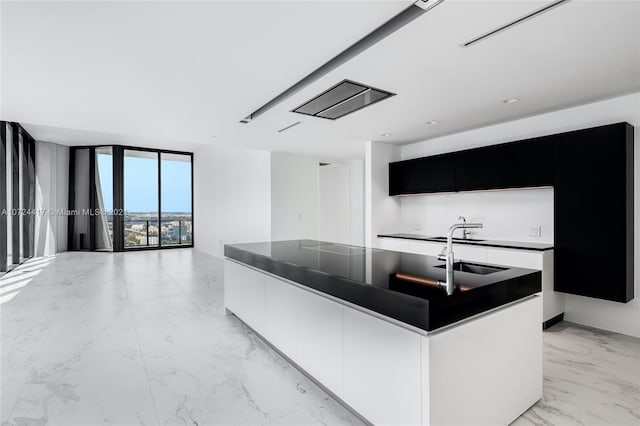 kitchen featuring light tile floors, a center island with sink, sink, and a wall of windows