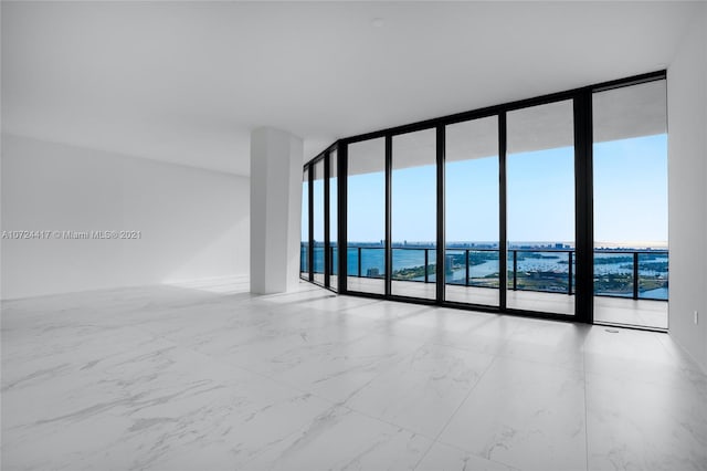 unfurnished room featuring a beach view, a water view, light tile flooring, and a wall of windows