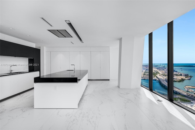 kitchen with sink, light tile floors, white cabinets, a water view, and a center island