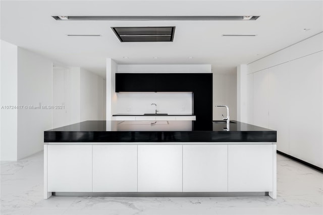 interior space featuring light tile floors, white cabinetry, and a kitchen island with sink