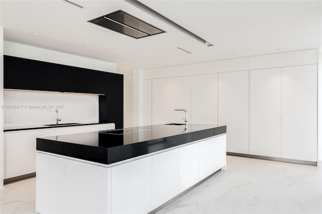 kitchen featuring white cabinets, a center island with sink, and sink