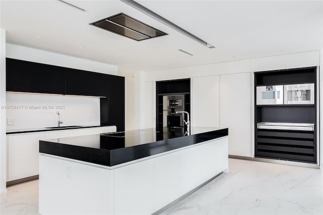 kitchen with white cabinetry, an island with sink, double oven, and sink