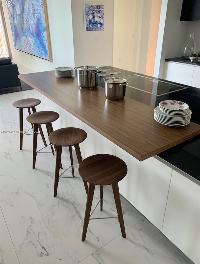 kitchen featuring stainless steel counters, a breakfast bar, light tile floors, and white cabinetry