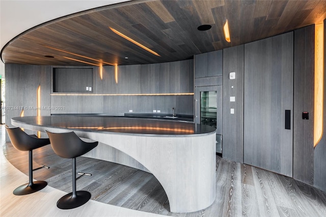 kitchen featuring a kitchen bar, wood walls, a center island, wooden ceiling, and dark hardwood / wood-style flooring