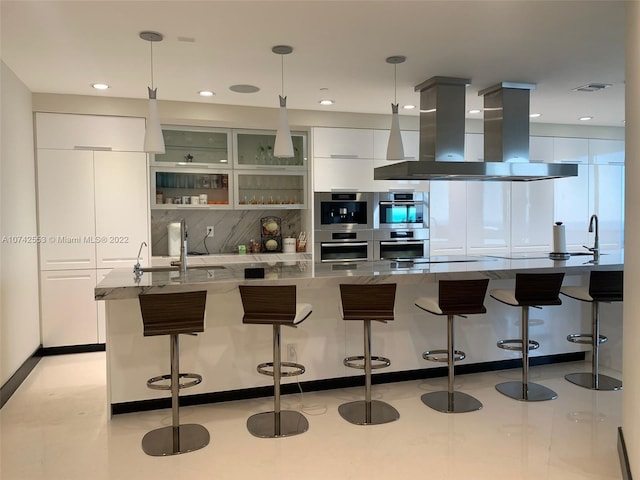 kitchen with double oven, white cabinetry, hanging light fixtures, island exhaust hood, and sink