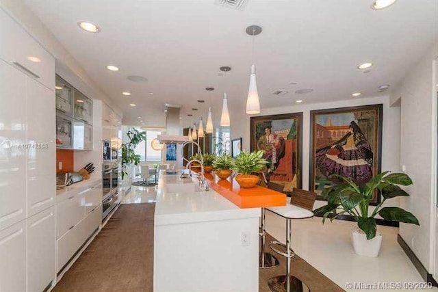 kitchen with decorative light fixtures, a kitchen breakfast bar, white cabinets, stainless steel oven, and island range hood