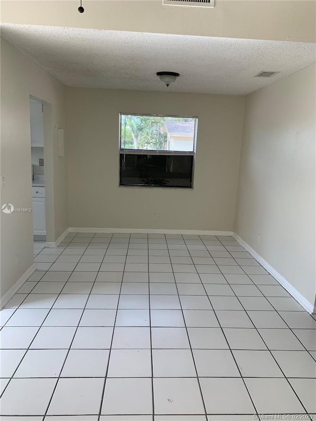 tiled empty room featuring a textured ceiling