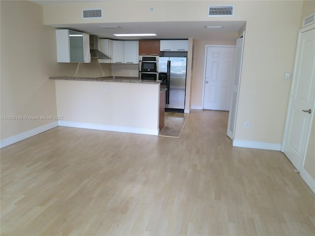 kitchen featuring stainless steel appliances, wall chimney exhaust hood, light wood-type flooring, and visible vents