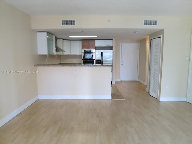 kitchen featuring stainless steel appliances, light wood-type flooring, a peninsula, and visible vents