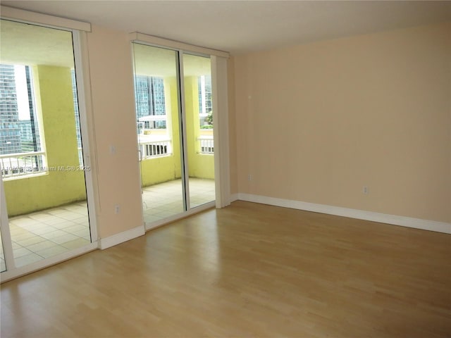 unfurnished room with a healthy amount of sunlight, floor to ceiling windows, baseboards, and wood finished floors