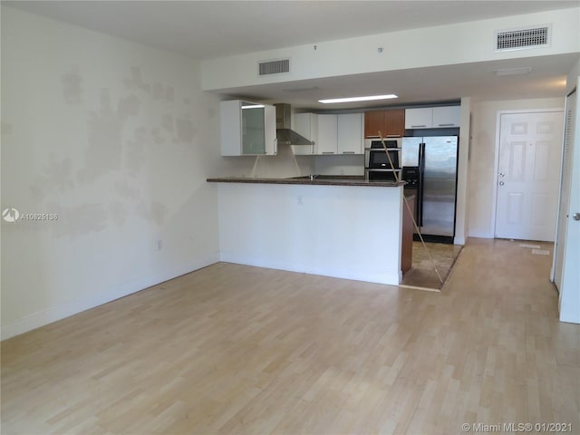 kitchen with a peninsula, visible vents, appliances with stainless steel finishes, wall chimney exhaust hood, and dark countertops