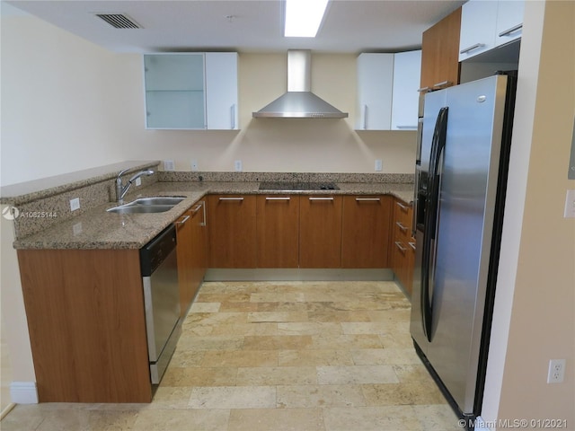 kitchen with wall chimney exhaust hood, a sink, appliances with stainless steel finishes, brown cabinetry, and light stone counters