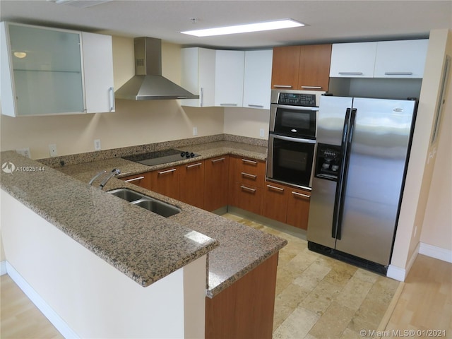 kitchen featuring wall chimney exhaust hood, brown cabinetry, a peninsula, appliances with stainless steel finishes, and a sink