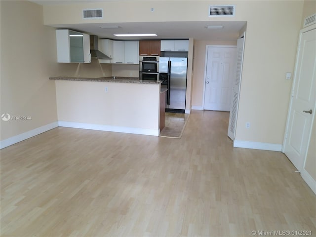 kitchen with stainless steel appliances, a peninsula, visible vents, and wall chimney exhaust hood