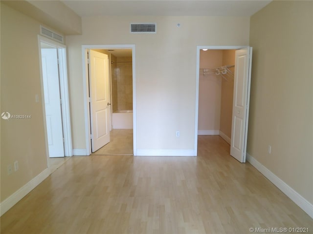 unfurnished bedroom with light wood-style flooring, a spacious closet, and visible vents