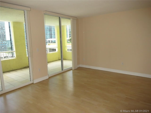 unfurnished room with floor to ceiling windows, plenty of natural light, baseboards, and wood finished floors