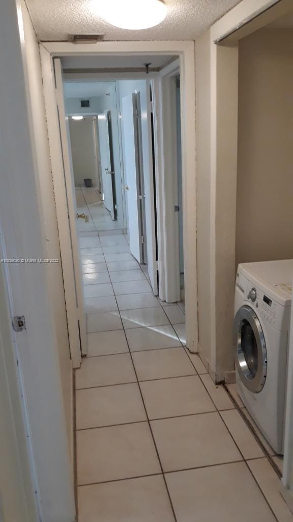 hall with light tile patterned floors, a textured ceiling, and washer / clothes dryer