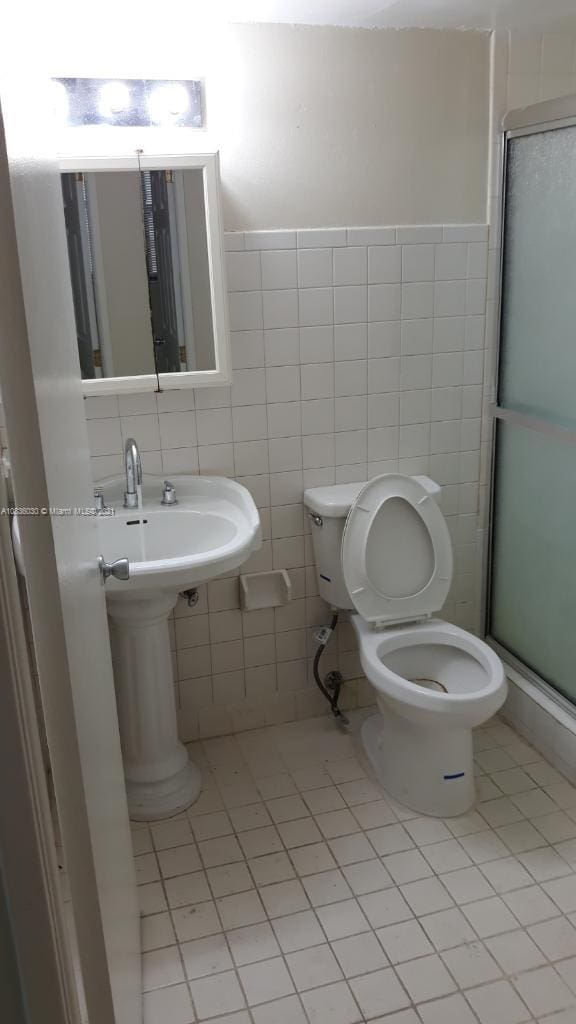 bathroom with tile patterned floors, toilet, a shower with shower door, and tile walls