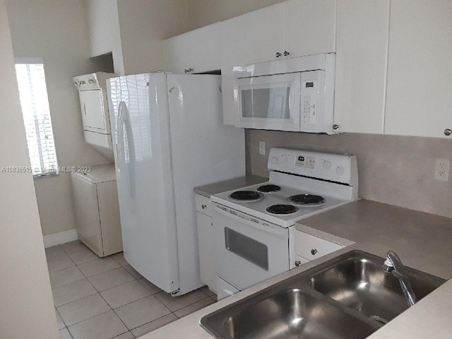 kitchen with sink, light tile patterned floors, stacked washer / dryer, white appliances, and white cabinets