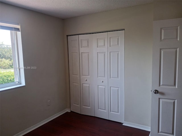 unfurnished bedroom featuring a textured ceiling, a closet, and dark wood-type flooring