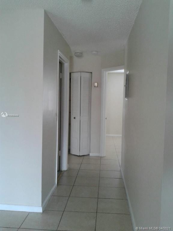 corridor with a textured ceiling and light tile patterned flooring