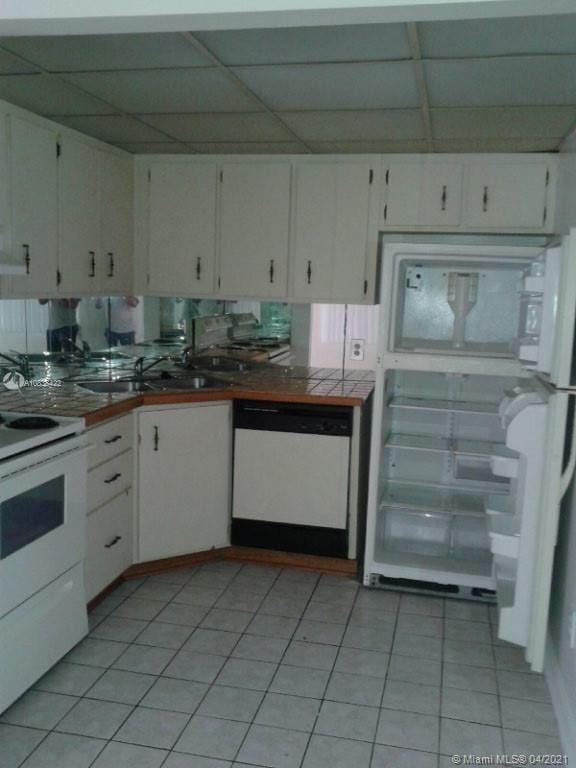 kitchen with a drop ceiling, white cabinetry, light tile patterned flooring, and white appliances