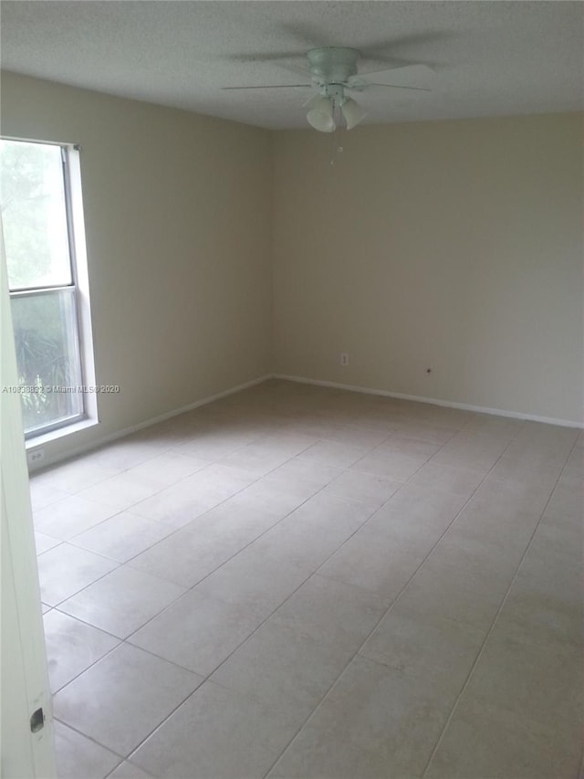 empty room featuring ceiling fan, light tile patterned floors, and a textured ceiling