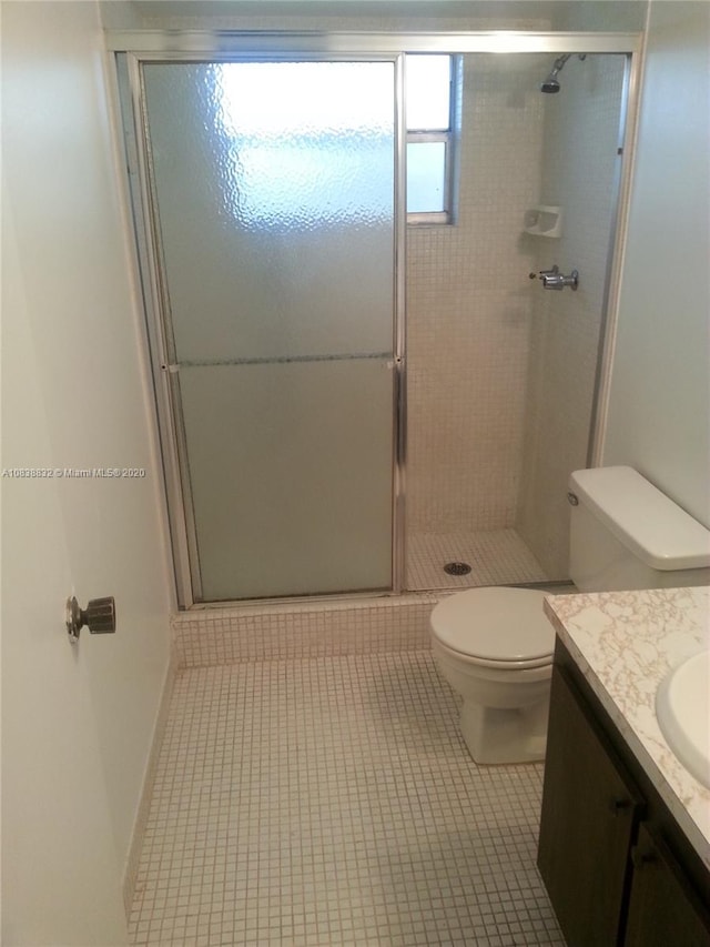 bathroom featuring toilet, vanity, tile patterned floors, and a shower with shower door