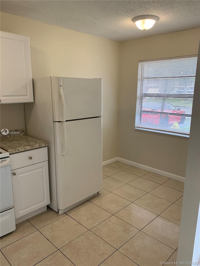 kitchen featuring white appliances, white cabinets, light stone countertops, a textured ceiling, and light tile patterned floors