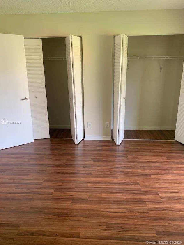 unfurnished bedroom featuring a textured ceiling, two closets, and dark wood-type flooring